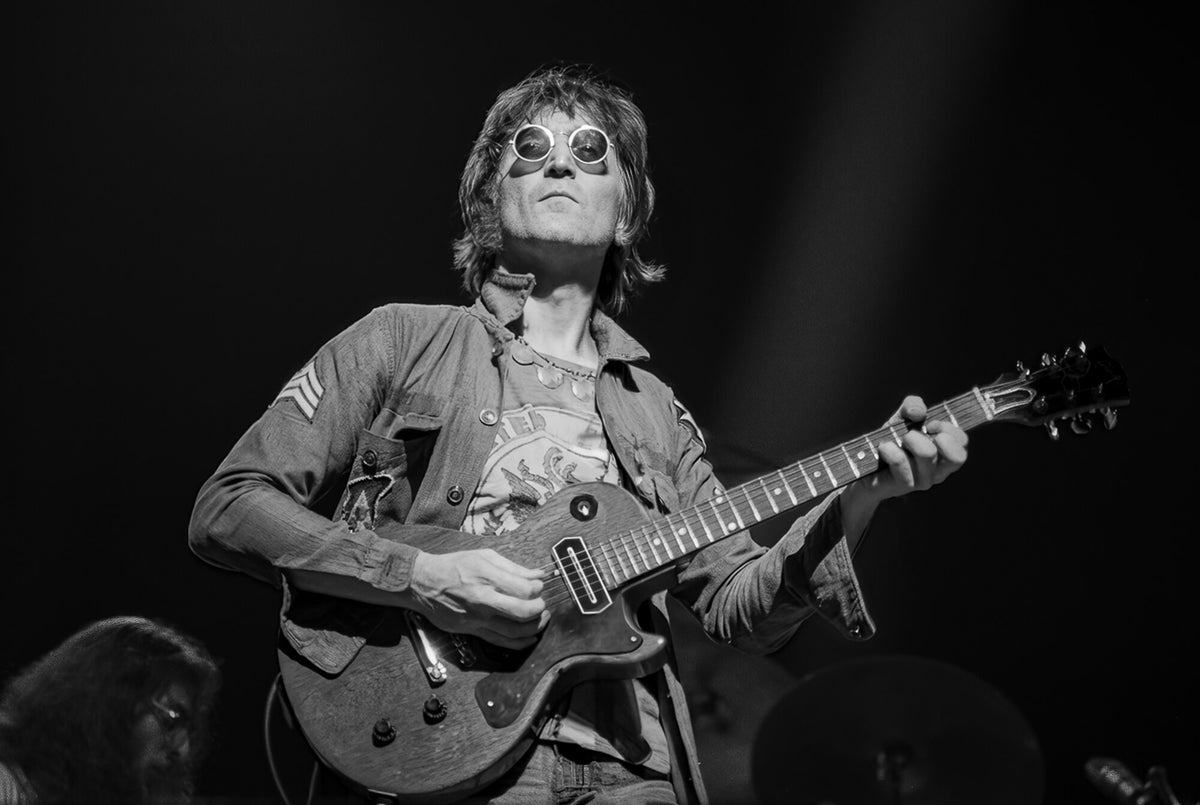 John Lennon performing with an electric guitar and round glasses, in black and white, 1972, photographed by Lynn Goldsmith.