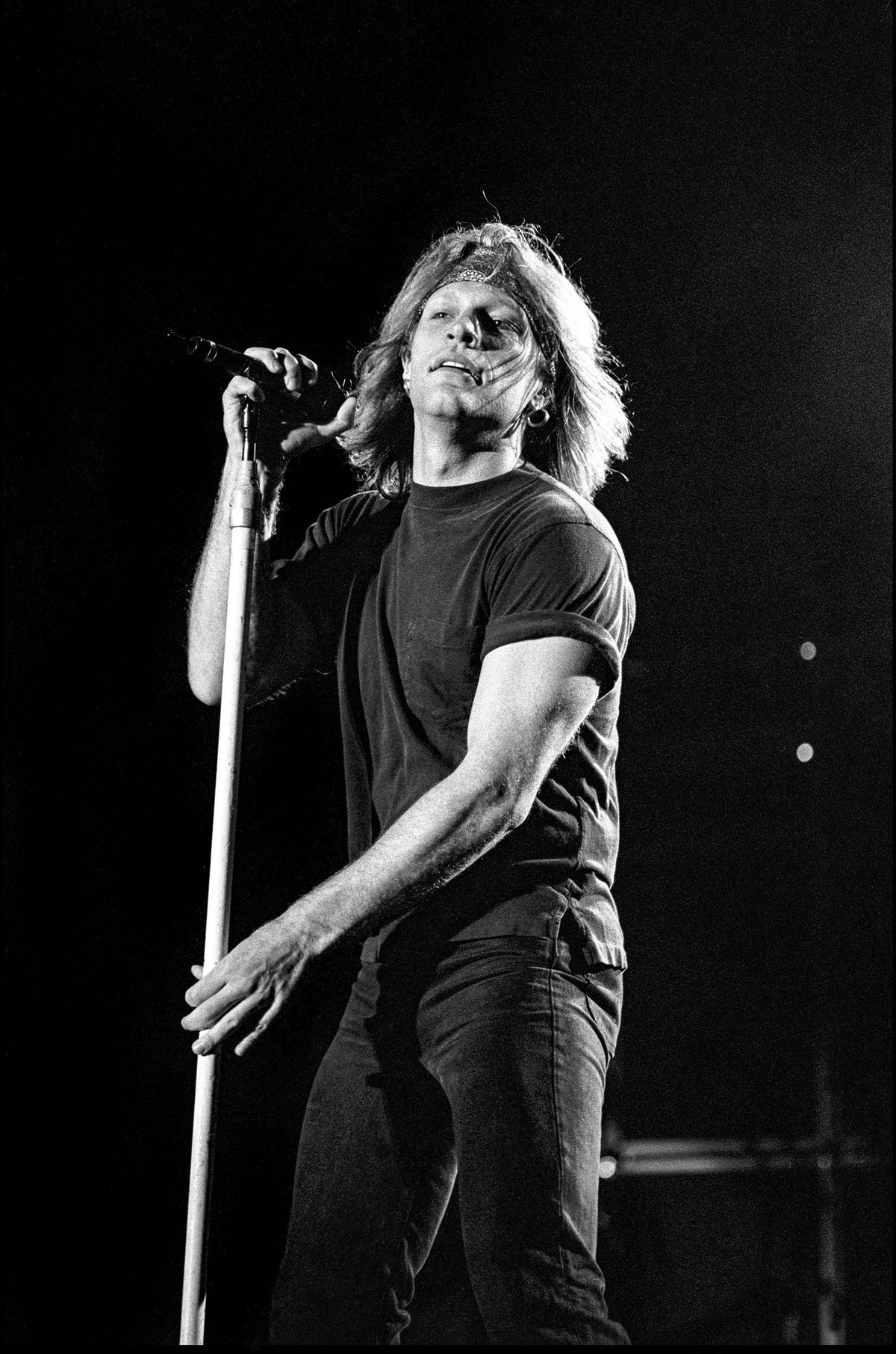 Jon Bon Jovi singing at a microphone stand in a dark T-shirt on stage at Jones Beach, Long Island, 1995, photographed by David Corio.