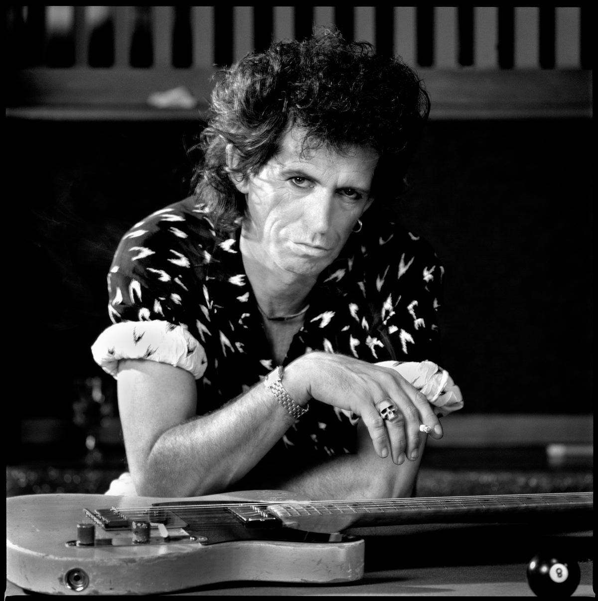 Keith Richards rests his arms on a pool table and looks directly toward the camera. Photograph by Timothy White, New York City, 1988.