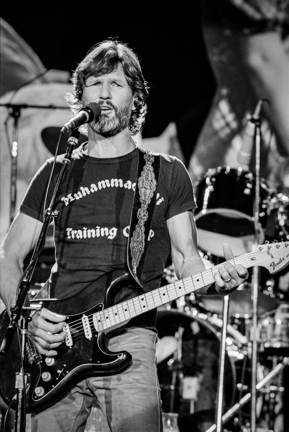 Kris Kristofferson singing with electric guitar on stage, in black and white, 1979, photographed by Lynn Goldsmith.