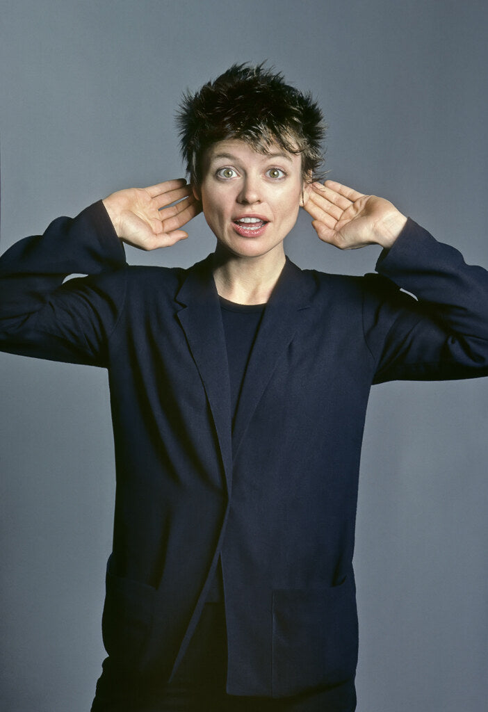 Laurie Anderson cupping her hands behind her ears, in color, 1982, photographed by Lynn Goldsmith.