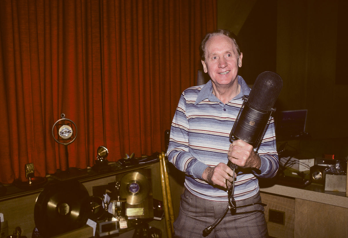 Les Paul in a striped sweater beside his equipment, in color, 1981, photographed by Lynn Goldsmith.