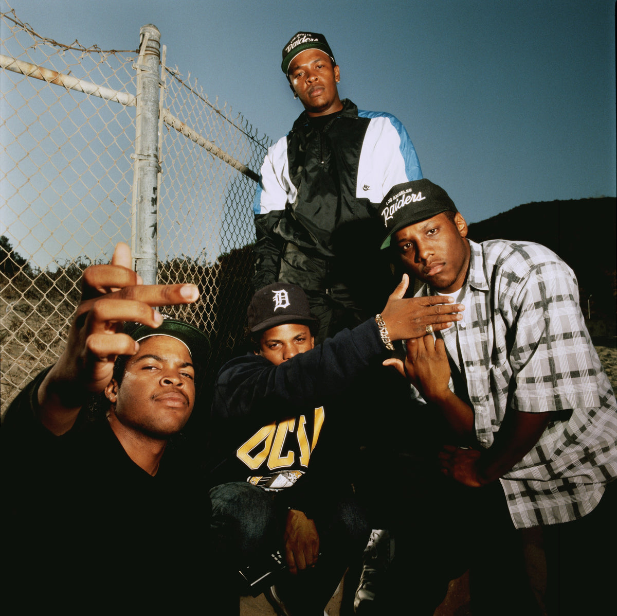 N.W.A gathers beside a chain-link fence in a low-angle group portrait. Photograph by Timothy White, Malibu, California, 1989.