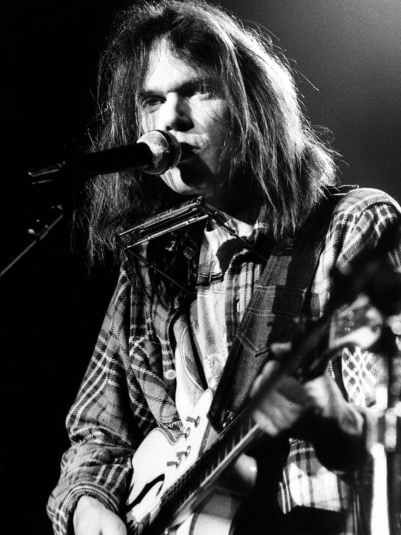 Neil Young singing at the microphone with guitar in 1976. Photograph by Gijsbert Hanekroot.