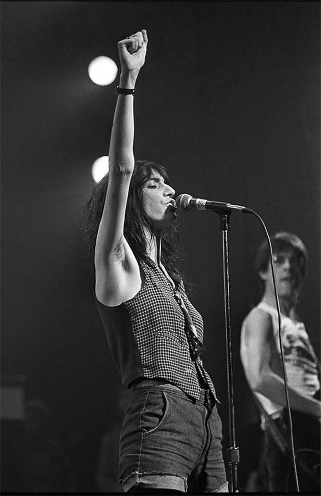 Patti Smith with one arm raised toward the stage light, photographed by Charlyn Zlotnik, 1977.