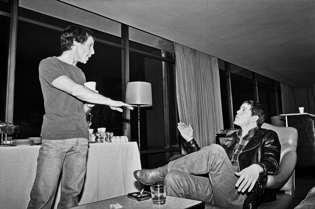 Paul Simon talking with Lou Reed by a window, in black and white, 1980, photographed by Lynn Goldsmith.