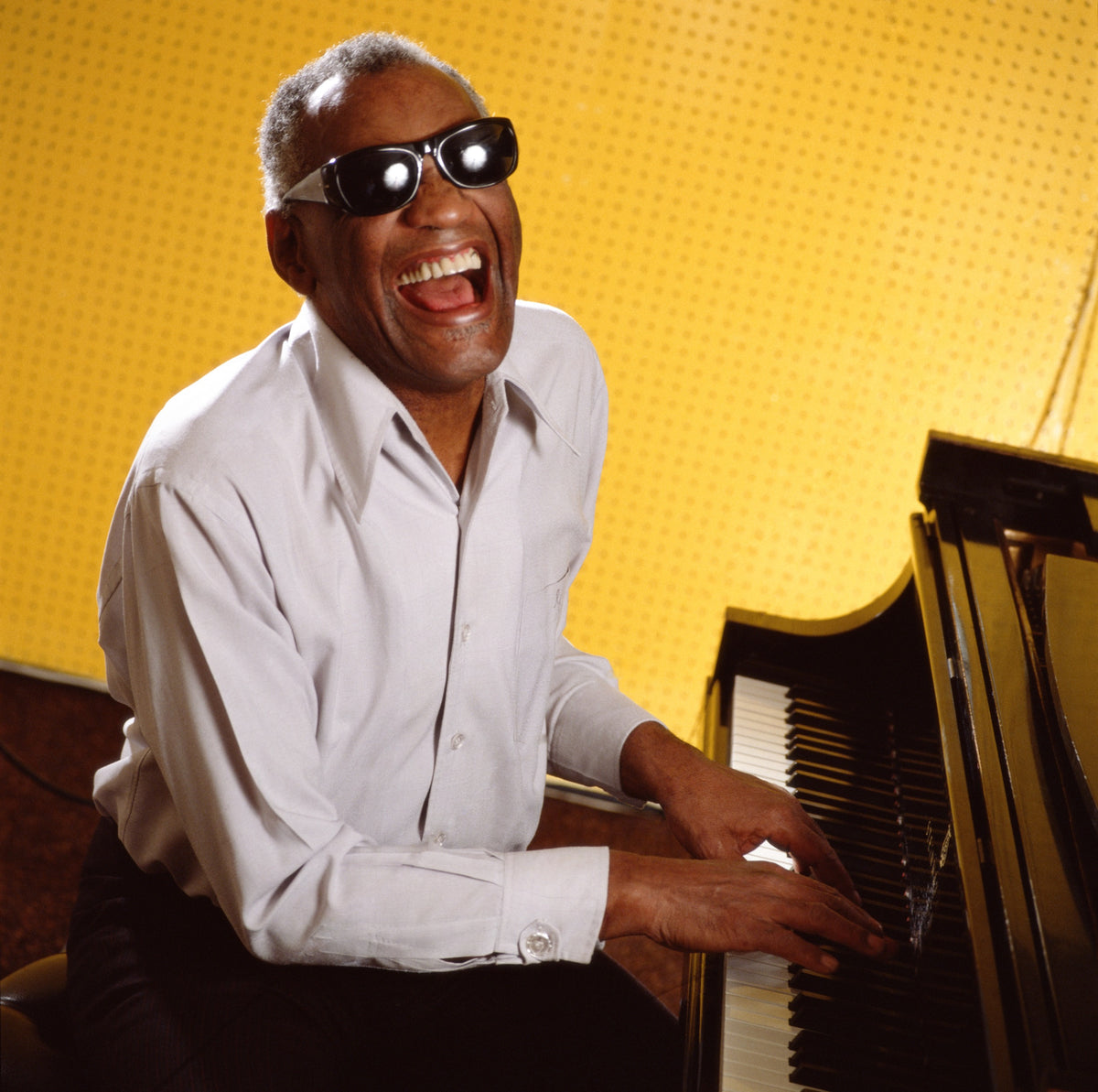 Ray Charles smiles at the piano against a bright yellow backdrop. Photograph by Timothy White, Los Angeles, California, 1988.