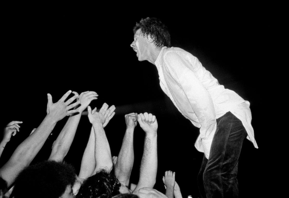 Ray Davies leaning toward the raised hands of the crowd, in black and white, 1978, photographed by Lynn Goldsmith.