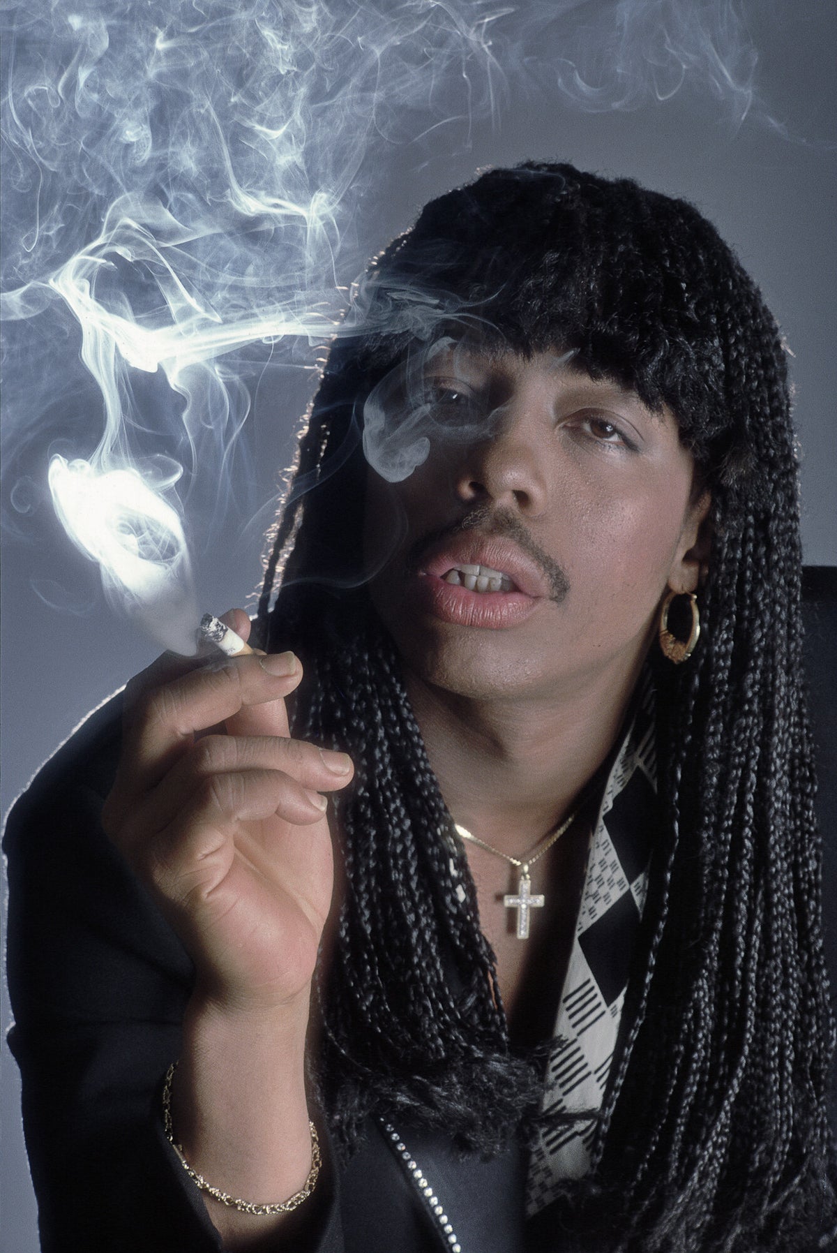 Rick James in long braids with cigarette smoke curling around him, in color, 1982, photographed by Lynn Goldsmith.