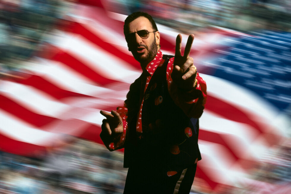 Ringo Starr flashing a peace sign before an American flag, in color, 1992, photographed by Lynn Goldsmith.