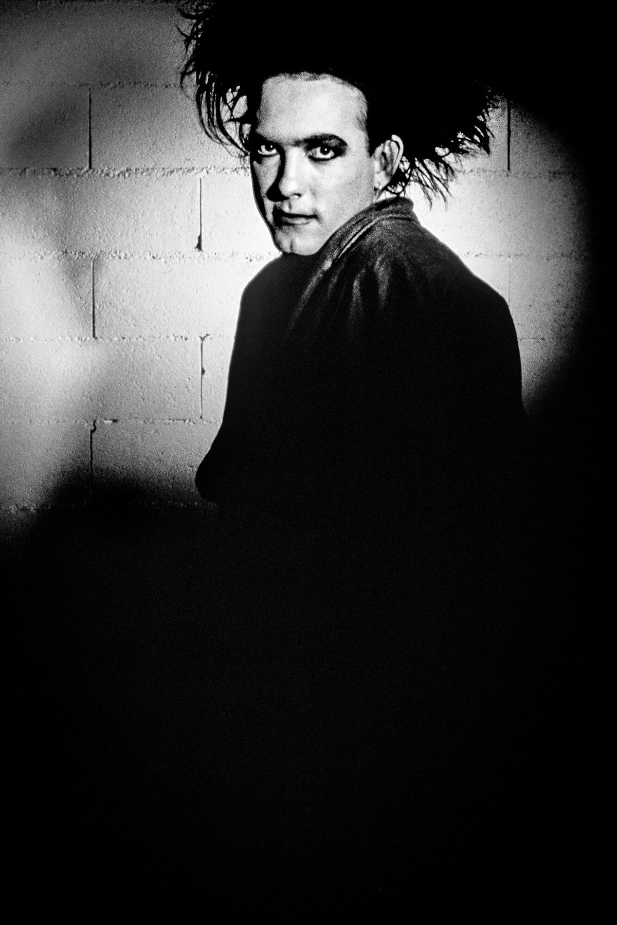 Robert Smith emerging from deep shadow, in black and white, 1986, photographed by Lynn Goldsmith.