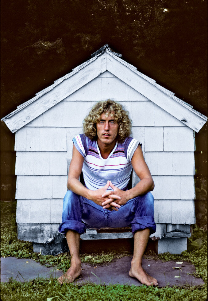 Roger Daltrey seated barefoot outside a small white shed, in color, 1978, photographed by Lynn Goldsmith.