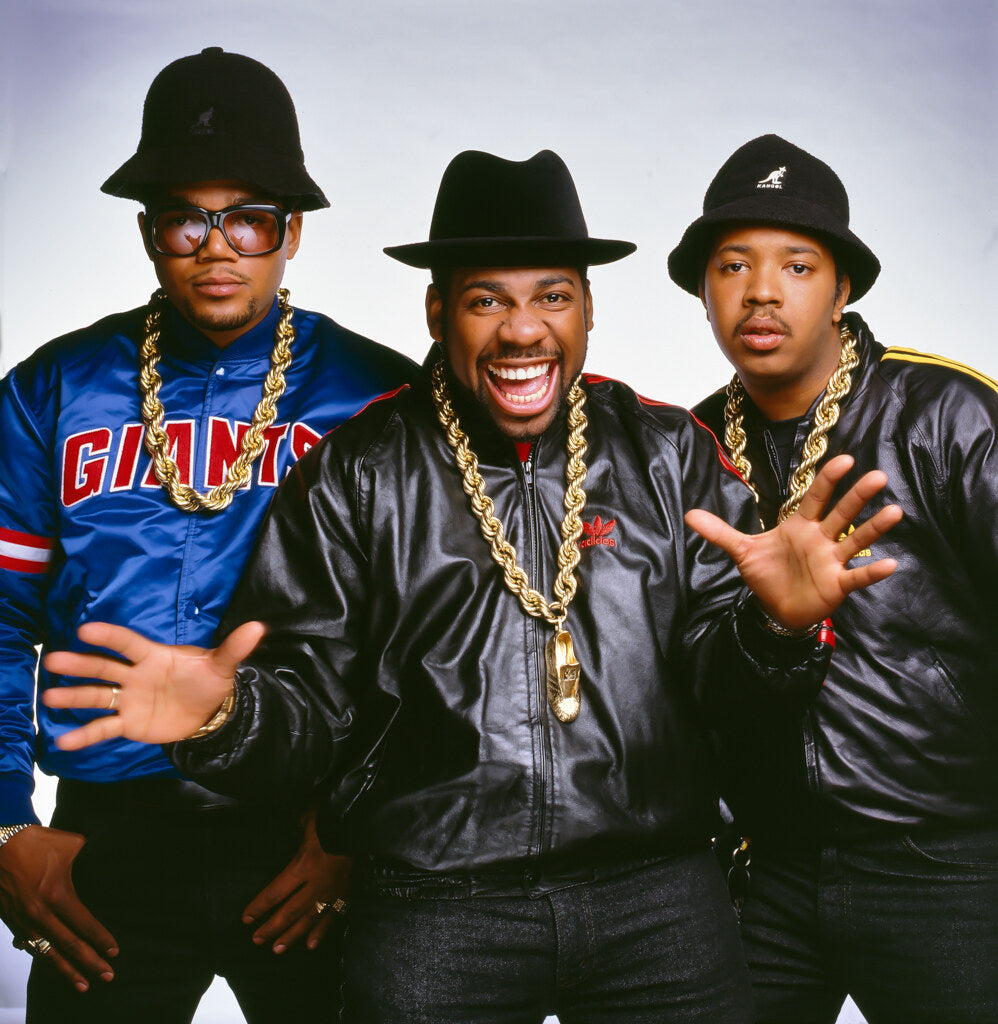 Run-DMC in fedoras and gold chains in a studio group portrait, in color, 1987, photographed by Lynn Goldsmith.
