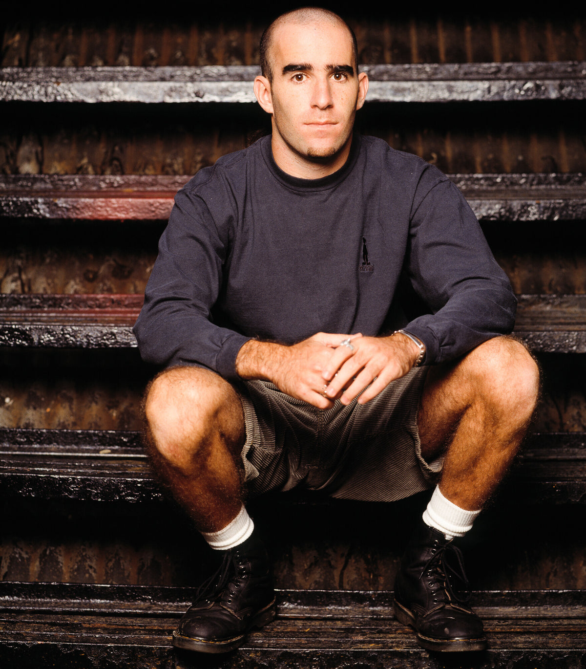 Scott Ian of Anthrax crouched on wooden steps, in color, 1991, photographed by Lynn Goldsmith.