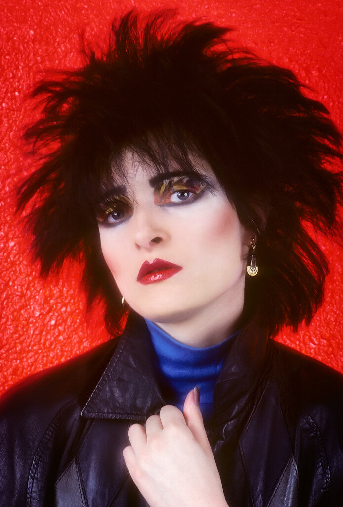 Siouxsie Sioux in strong makeup against a red background, in color, 1980, photographed by Lynn Goldsmith.