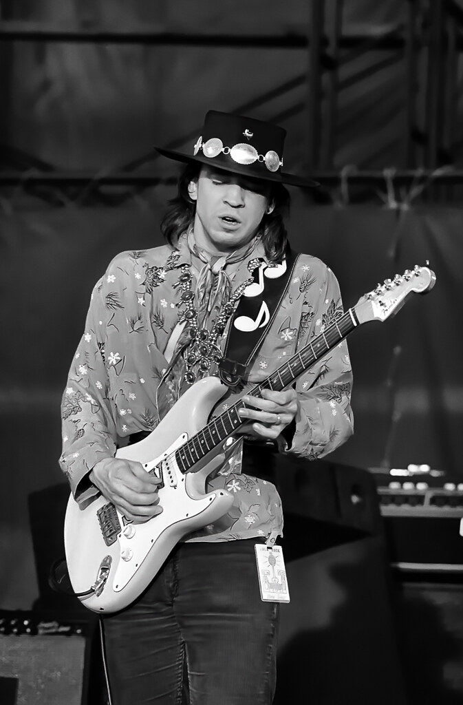 Stevie Ray Vaughan playing guitar in a flat-brimmed hat, in black and white, 1983, photographed by Lynn Goldsmith.
