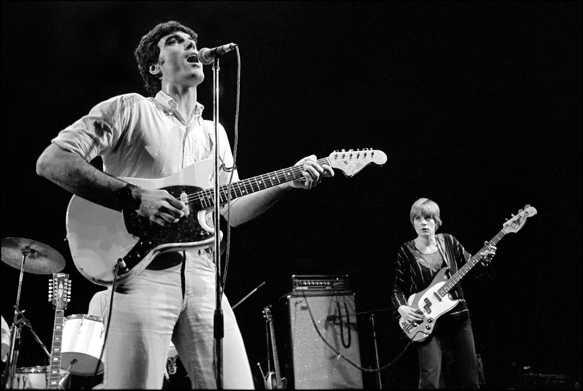 David Byrne singing and playing guitar with Tina Weymouth on bass behind him, on stage at The Roundhouse, London, 1978, photographed by David Corio.