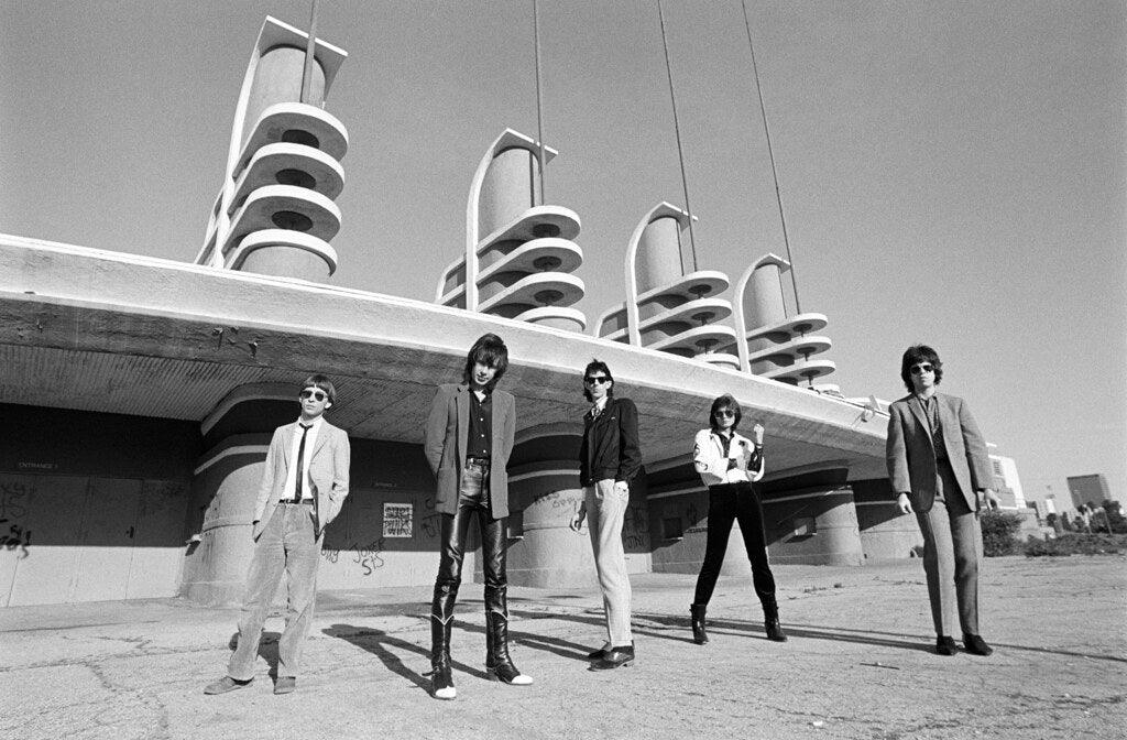 The Cars standing before a streamlined white building, in black and white, 1980, photographed by Lynn Goldsmith.