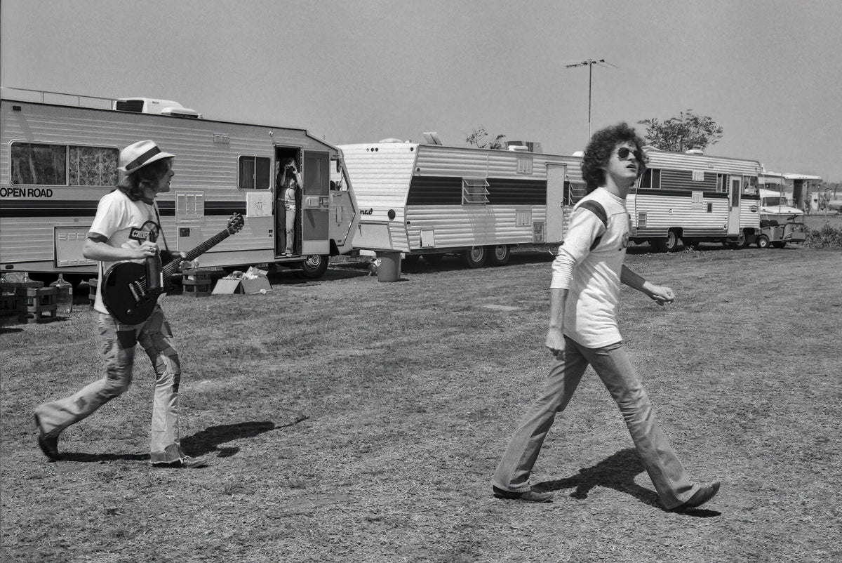 Two members of the Eagles walking past trailers, in black and white, 1974, photographed by Lynn Goldsmith.