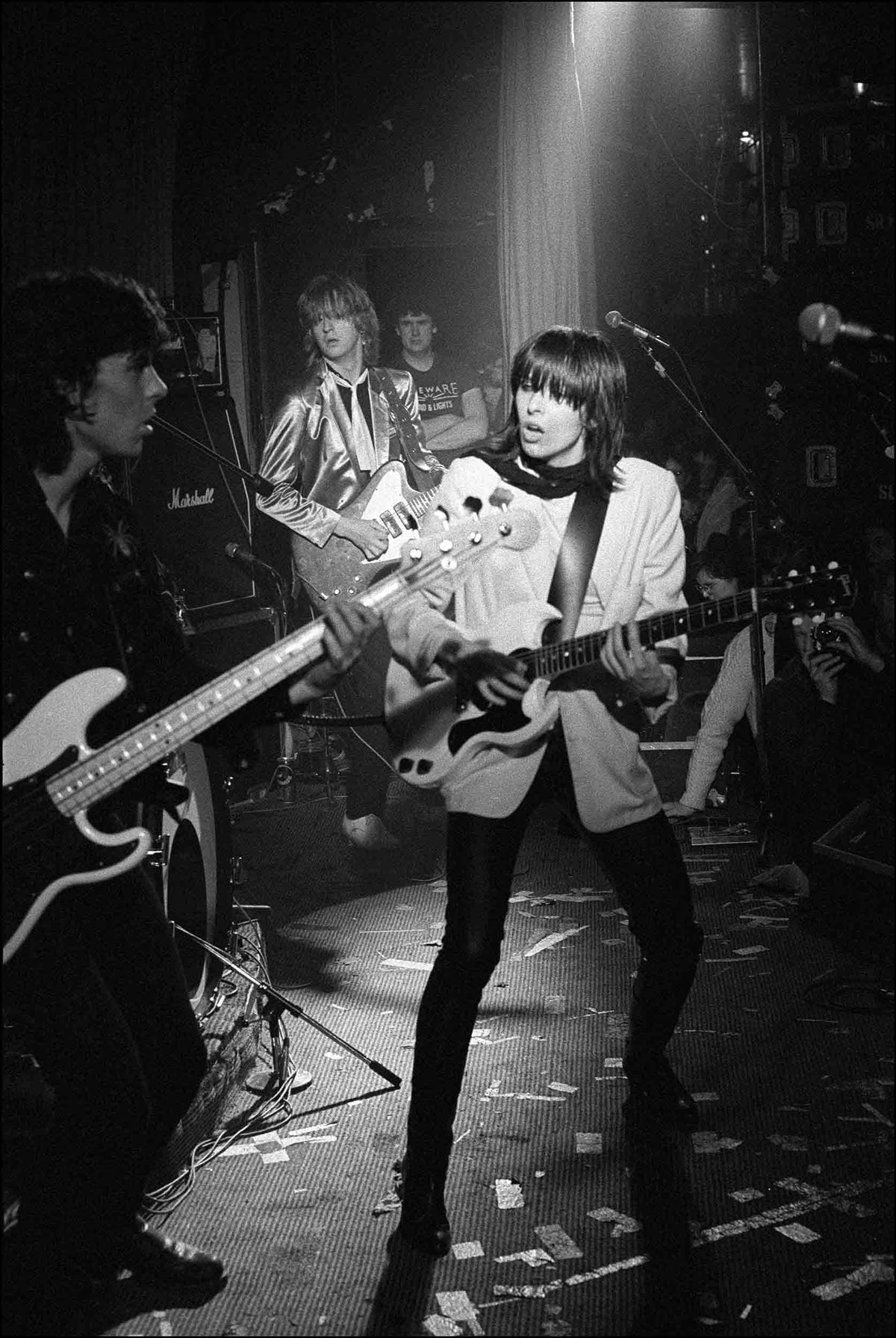 Chrissie Hynde playing a Gibson SG guitar with Pete Farndon and James Honeyman-Scott on stage at the Nashville Rooms, London, 1979, photographed by David Corio.