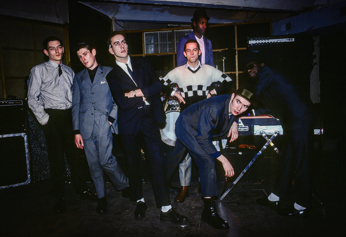 The Specials posing in suits in a dim room, in color, 1980, photographed by Lynn Goldsmith.