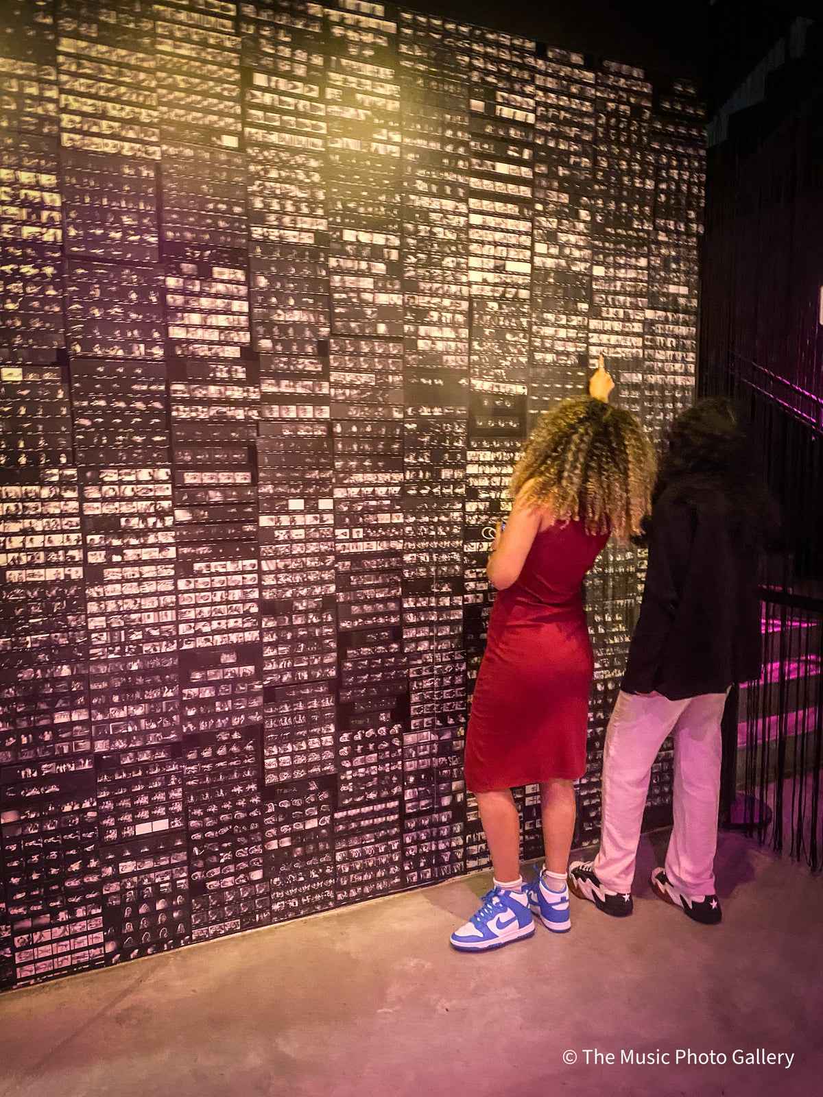 Visitors at a wall covered with small black-and-white photographs in Tina Turner: A Journey to the Future at the Museum of Image and Sound (MIS), São Paulo, Brazil.