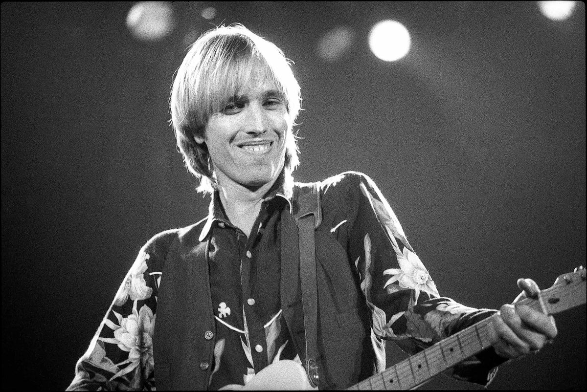 Tom Petty smiling on stage with his guitar in a floral shirt, Wembley, London, 1982, photographed by David Corio.