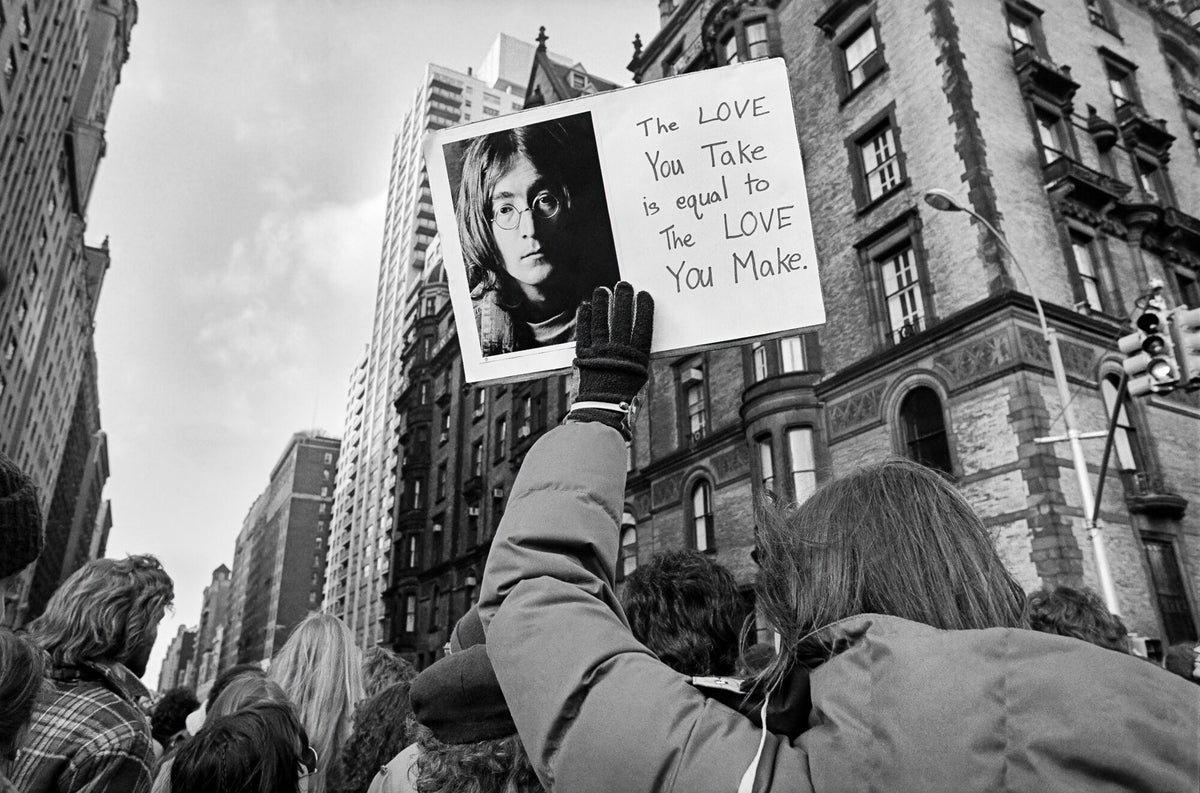 Mourners outside the Dakota holding a sign with John Lennon's portrait, 1980, photographed by Lynn Goldsmith.