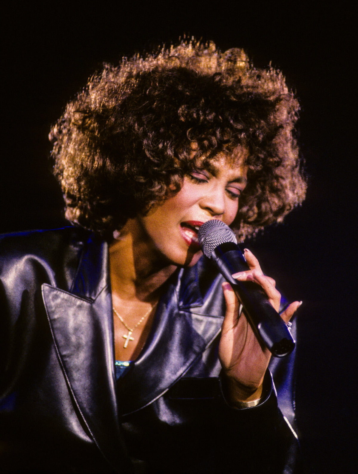 Whitney Houston singing with eyes closed in a purple jacket, in color, 1986, photographed by Lynn Goldsmith.