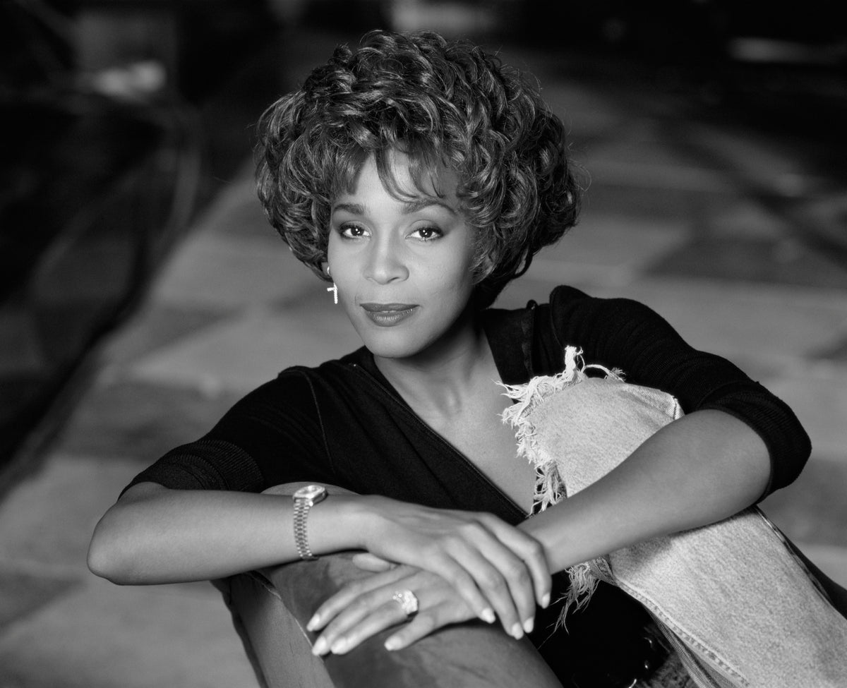 Whitney Houston rests her arms across a chair in a closely framed seated portrait. Photograph by Timothy White, New York City, 1990.